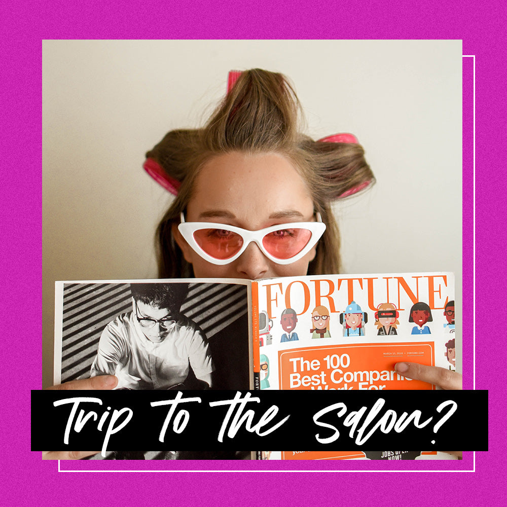 Woman with glasses reading a magazine at a hair salon with rollers in her hair