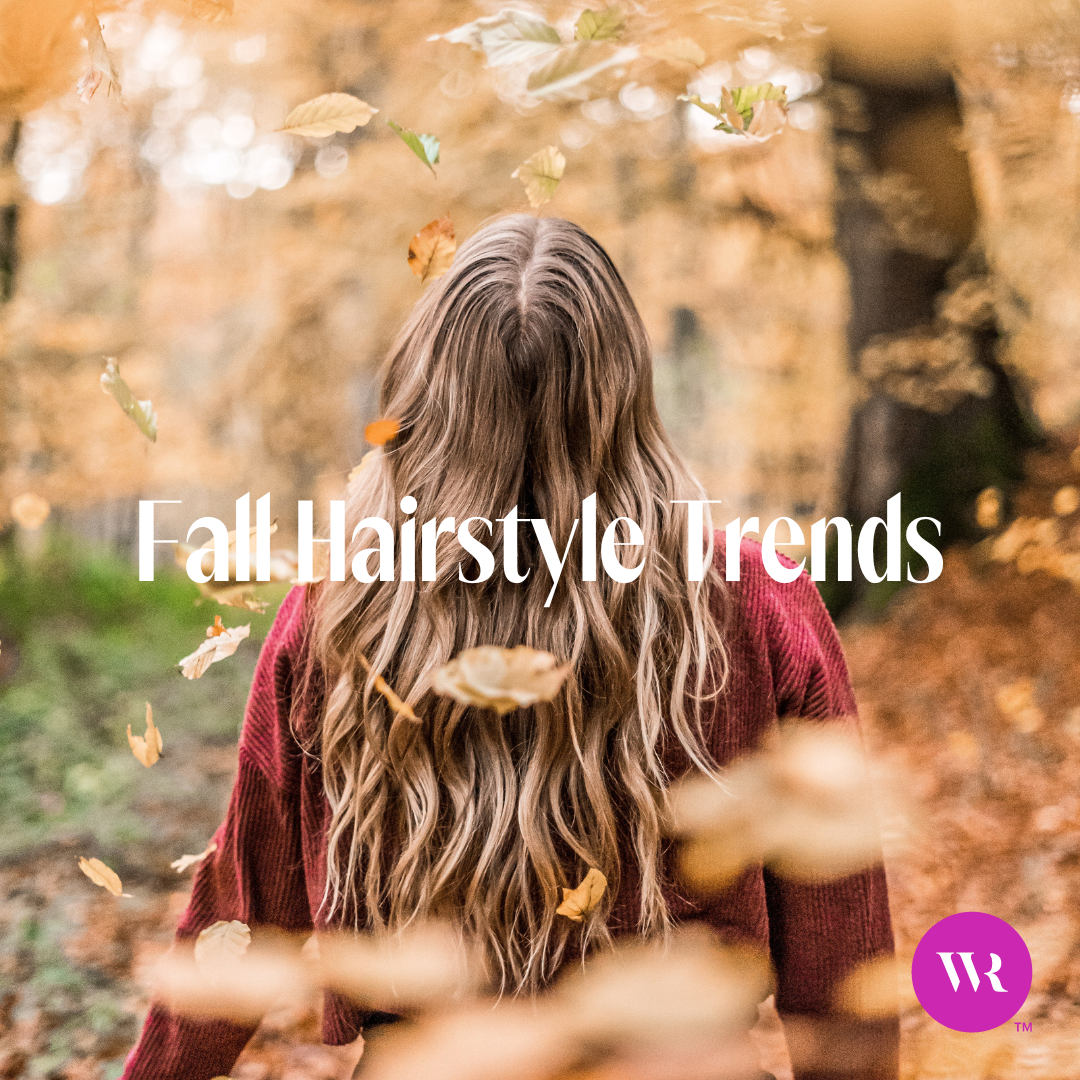 The back of a woman's head who has flowing wavy hair in a forest during fall with brown leaves falling