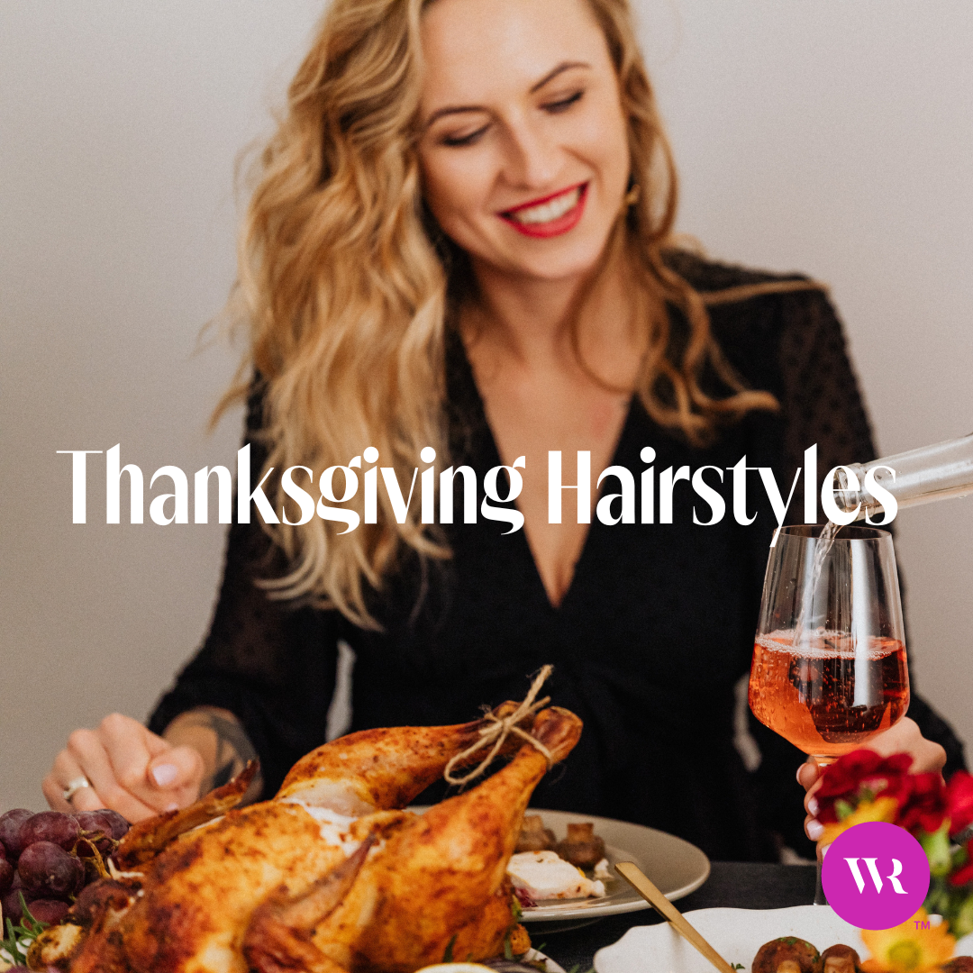 A happy woman with flowing hair sitting at a thanksgiving table with turkey, wine, and potatoes