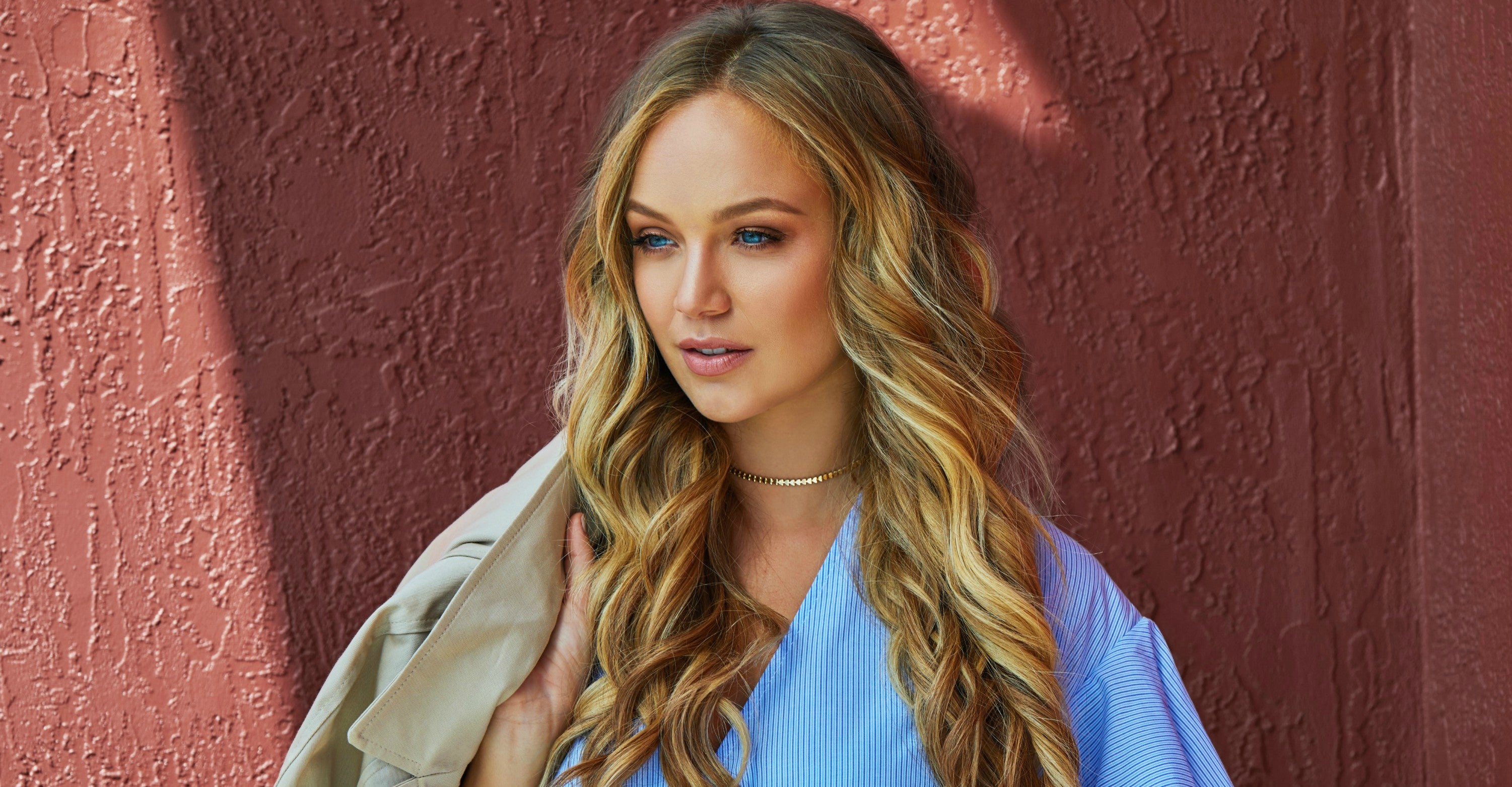 Woman with blonde hair extensions in a blue blouse with a jacket over her shoulder